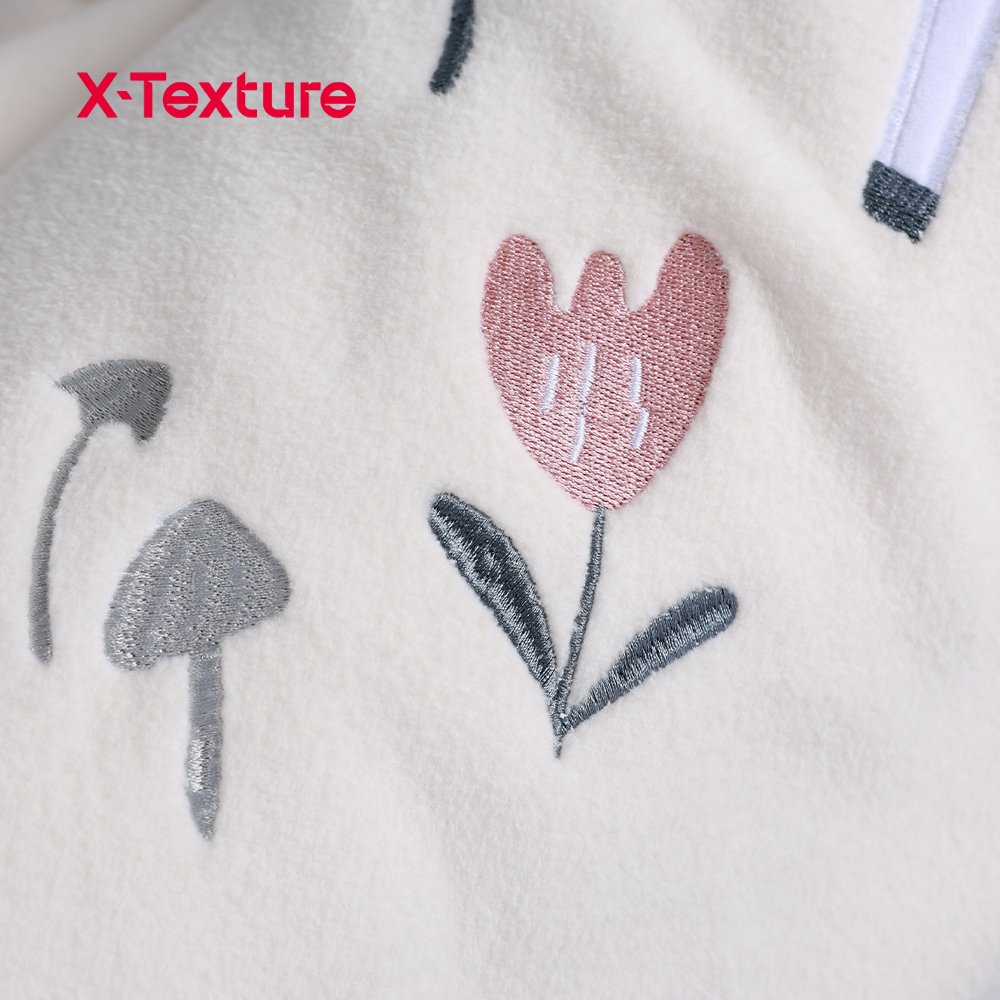 تصوير مقرب لتفاصيل التطريز الزهري على قماش صوف وحيد القرن أبيض كريمي.